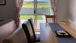 Ein Zimmer mit einer Schiebetür zum Balkon, einem Holztisch mit Tischdecke und einem Sofa.
