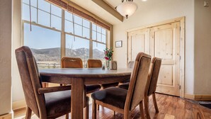 Un comedor con una mesa y sillas de madera, una ventana con vistas a montañas y una puerta con una lámpara.