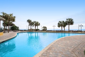 A swimming pool with a curved edge, surrounded by lounge chairs and palm trees. - 17th-floor oceanfront condo with pool, hot tub, WiFi & beach location (Myrtle Beach)