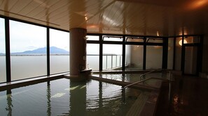 A large indoor swimming pool with a view of a body of water and mountains.