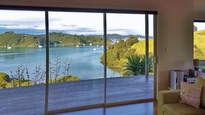 A room with large windows offering a view of a lake and hills. - Magic Water Views Russell (Russell)