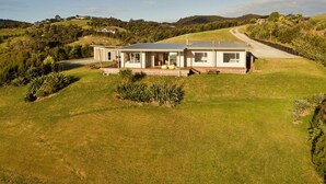 A modern house with a large deck, surrounded by a well-maintained lawn and hills in the background. - Magic Water Views Russell (Russell)