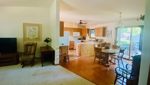 A spacious living room with a large TV, a dining area with wooden chairs, and a kitchen with wooden cabinets and a central island. - Walking distance to historic Arnold’s Park and West Lake Okoboji (Arnolds Park)
