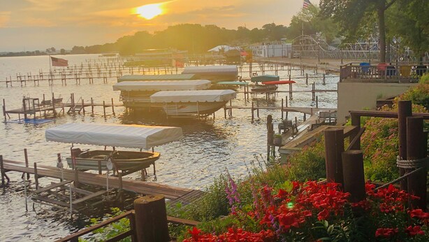 A waterfront area with boats docked, a flag, and a view of the sunset. - Walking distance to historic Arnold’s Park and West Lake Okoboji (Arnolds Park)