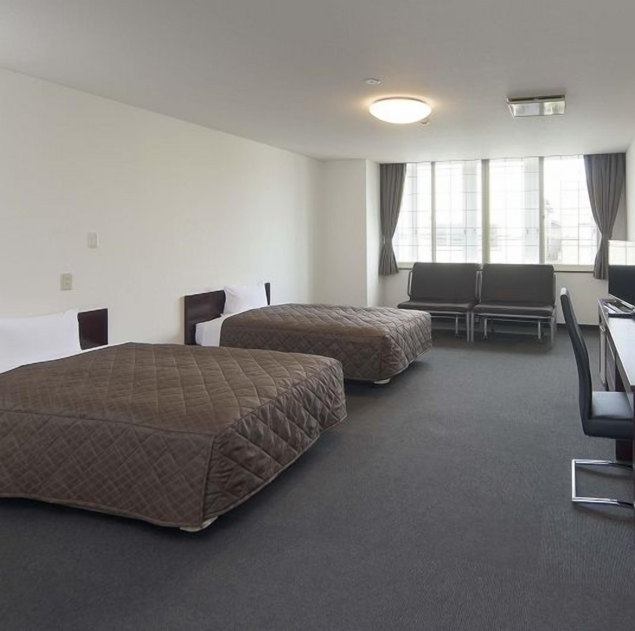 Habitación de hotel con dos camas, un escritorio, una silla y una ventana con cortinas.