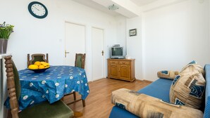 A living room with a dining table, a sofa, a television, and a clock on the wall. - Guesthouse Home Sweet Home - Standard One-Bedroom Apartment with Balcony (Dubrovnik)