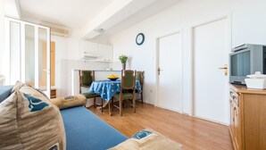 A compact living space with a sofa, a dining table with chairs, a television, and a kitchen area. - Guesthouse Home Sweet Home - Standard One-Bedroom Apartment with Balcony (Dubrovnik)