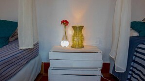 Un dormitorio con dos camas, una mesita de noche con un florero y una lámpara, y una cortina en la ventana.