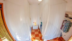 Un pasillo estrecho con cortinas blancas, suelo a cuadros, una mesita de noche con una lámpara y un perchero.