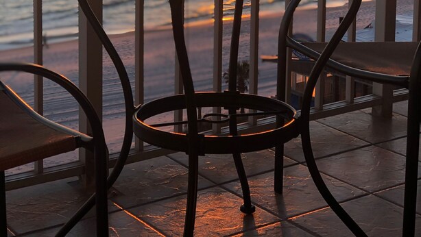 Mesa para dos con vasos y una taza, con vista al océano al atardecer.