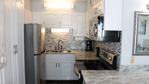 Una cocina moderna con armarios blancos, un refrigerador de acero inoxidable, un lavamanos doble, un microondas y una estufa.