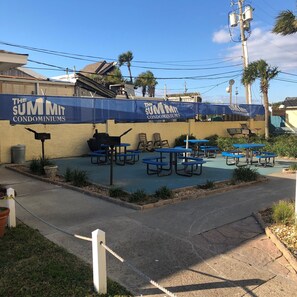 A fenced outdoor area with picnic tables and chairs, a barbecue grill, and a sign for "The Summit Condominiums".
