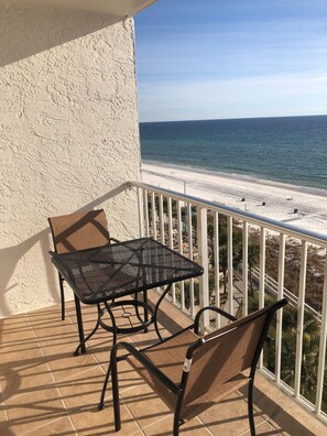 A balcony with a table and two chairs, overlooking a beach with a clear view of the ocean.