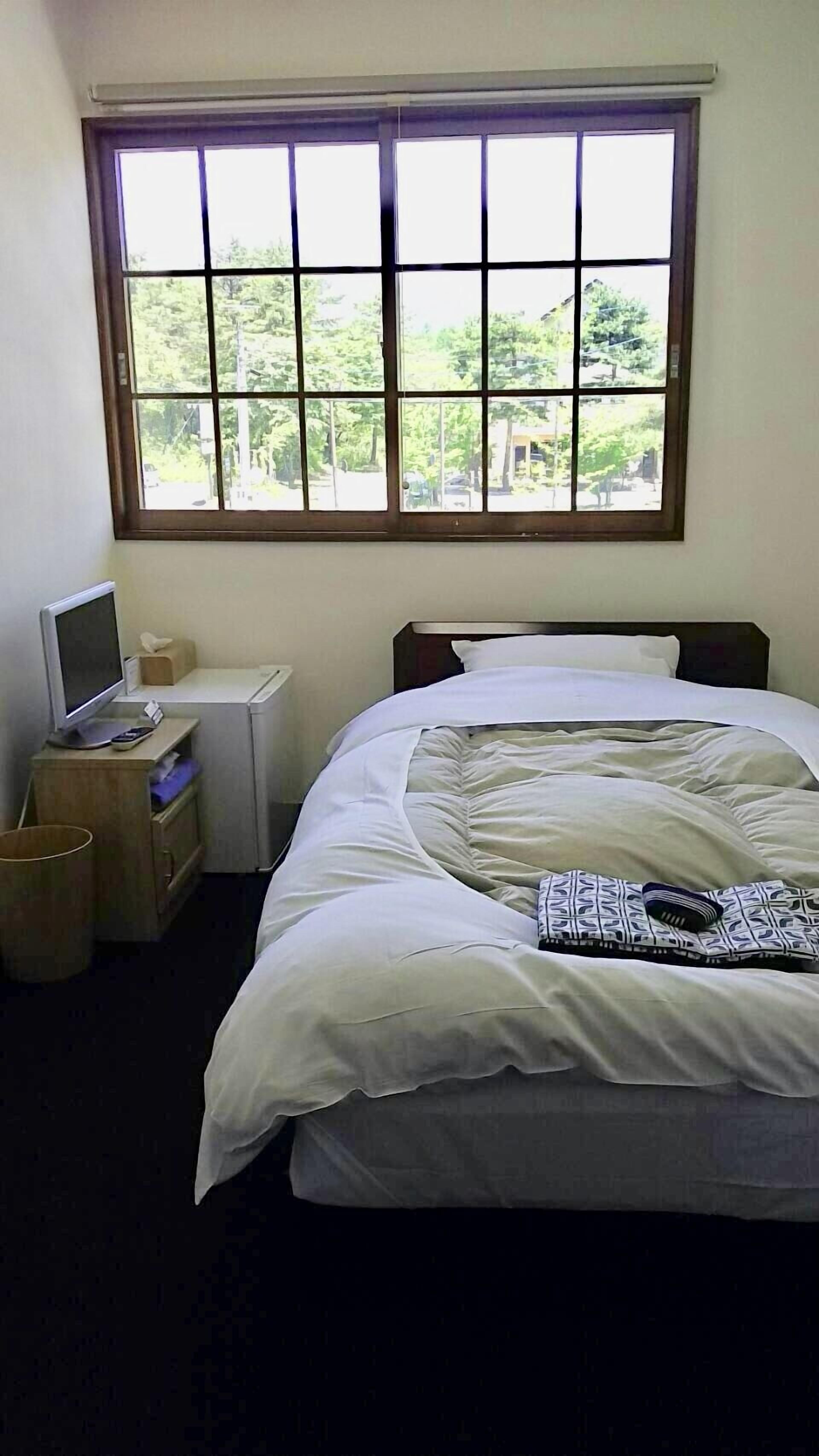 Un dormitorio con cama, escritorio, silla, ventana y vistas al exterior.