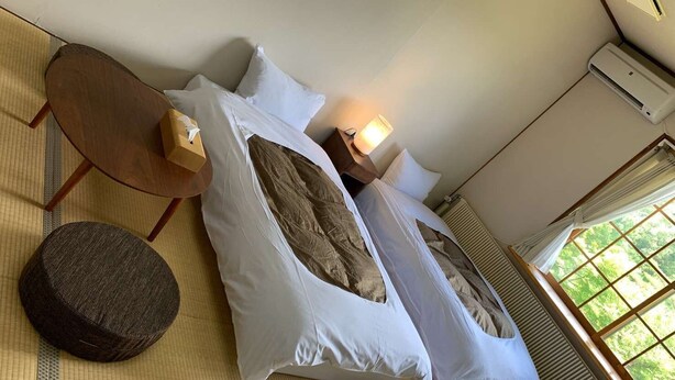 A room with a bed, a round ottoman, a small wooden table, and a window with a view of greenery. - Saizu Resort Hotel Urabandai (Kitashiobara)