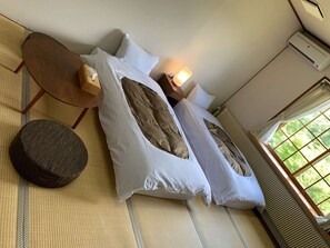 A room with a bed, a round ottoman, a small wooden table, and a window with a view of greenery. - Saizu Resort Hotel Urabandai (Kitashiobara)