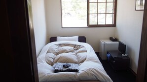A small, neatly made bed with white bedding and a patterned pillow, a bedside table with a remote control, a television, and a window with blinds. - Saizu Resort Hotel Urabandai (Kitashiobara)