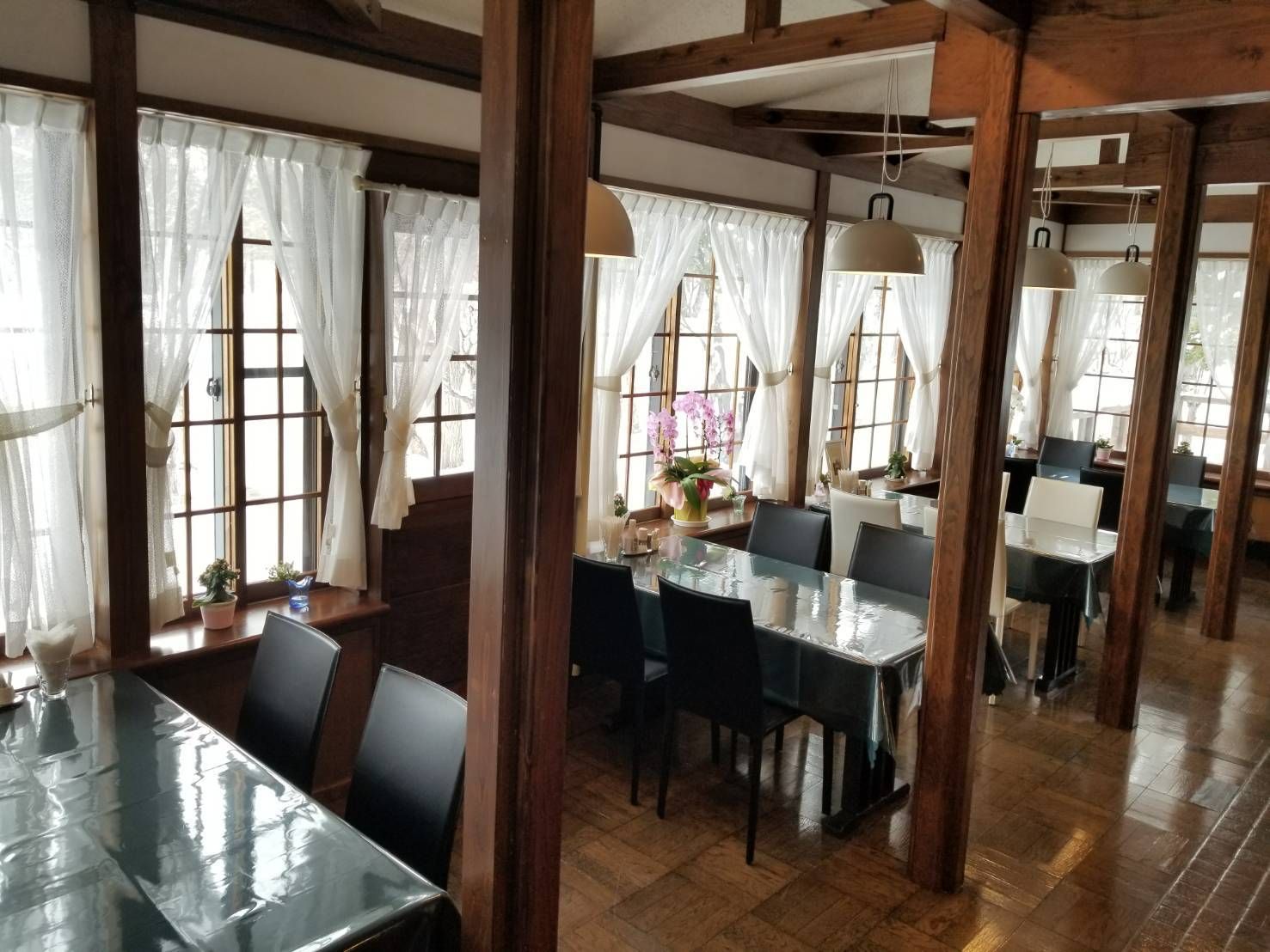 Un restaurante con vigas de madera, ventanas amplias con cortinas traslúcidas y una mesa central con sillas.