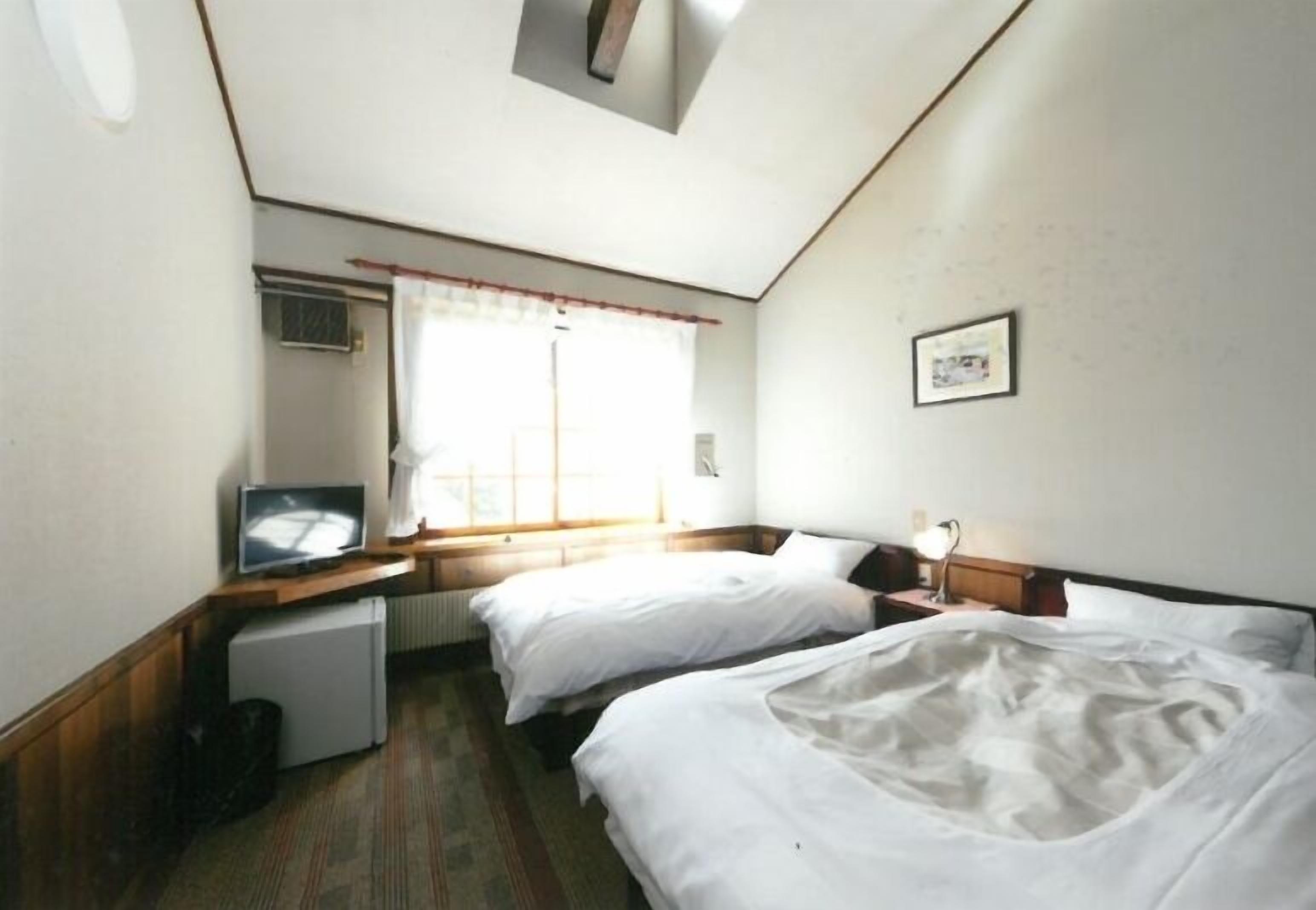 Habitación de hotel con dos camas, televisión, refrigerador pequeño y ventana con cortinas.