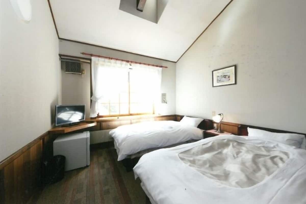 Een hotelkamer met twee bedden, een televisie, een kleine koelkast en een raam met gordijnen.