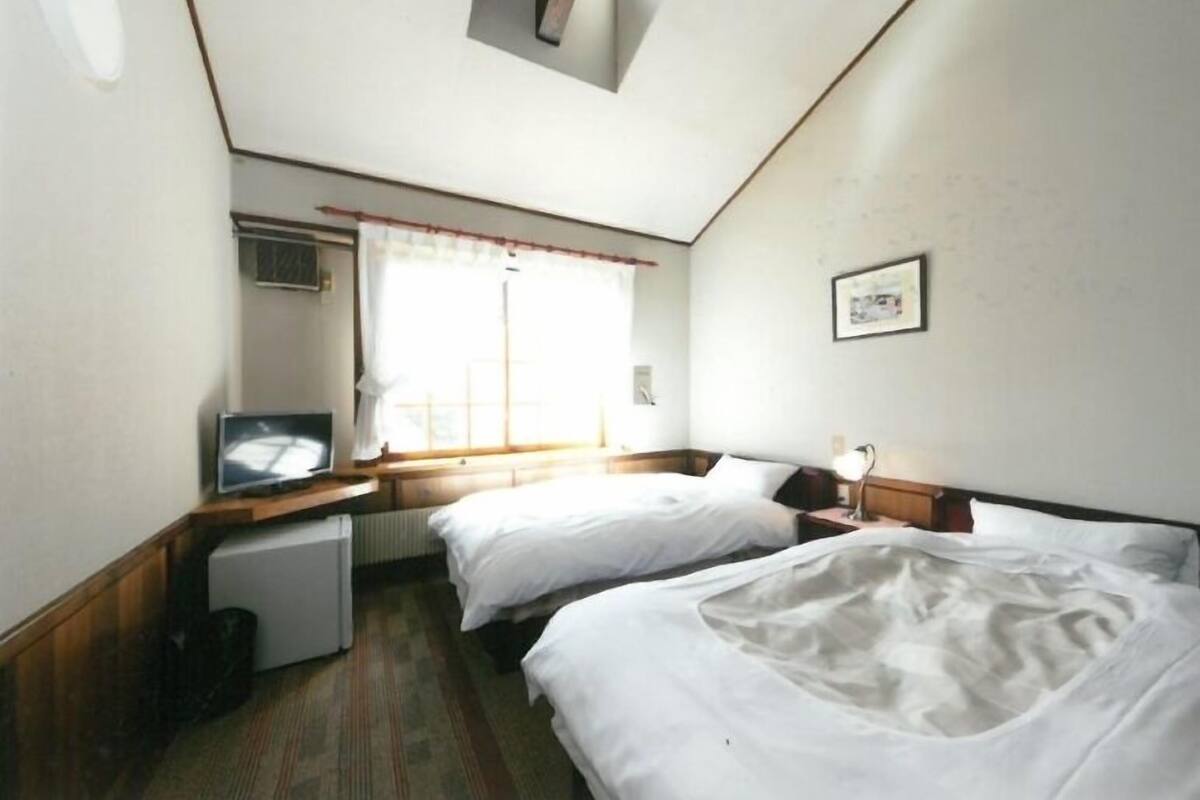 Een hotelkamer met twee bedden, een klein bureau met een televisie, een radiator en een raam met gordijnen.