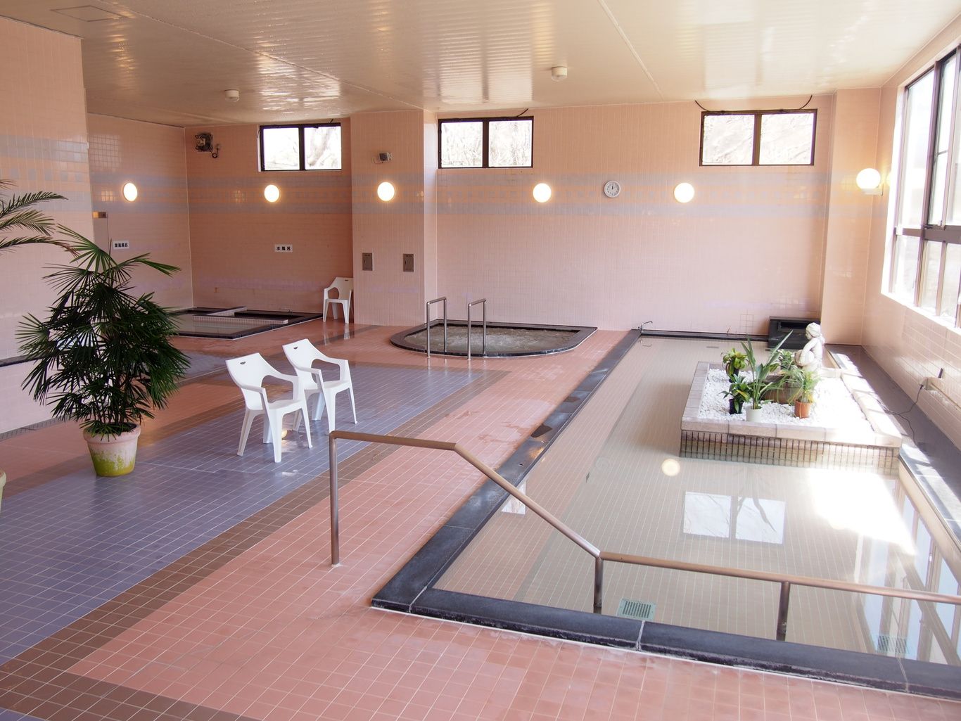Un área de piscina interior amplia con varias zonas de estar, una fuente central y plantas en macetas.