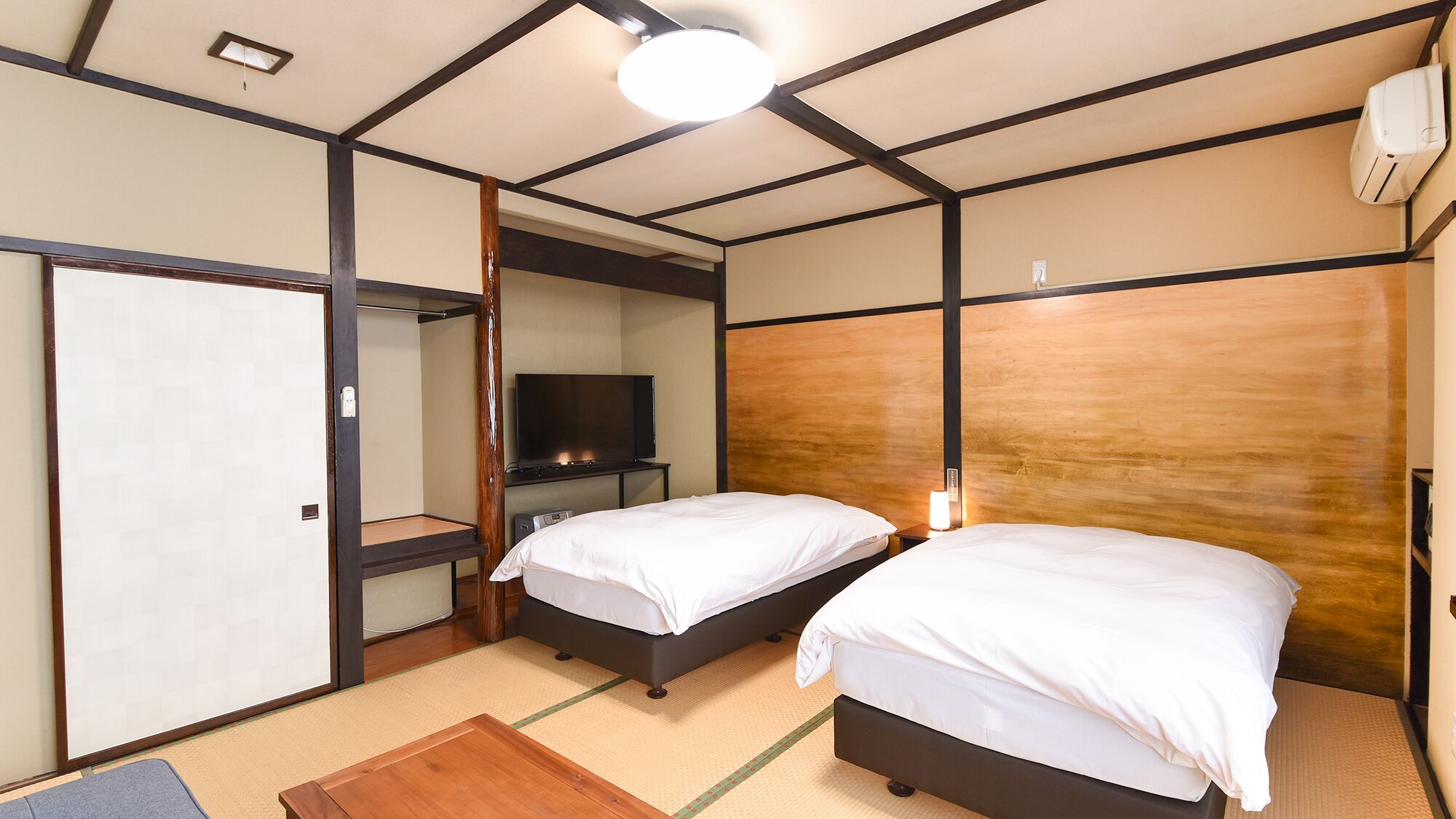 Una habitación de hotel con dos camas, televisión, armario y una lámpara en el techo.