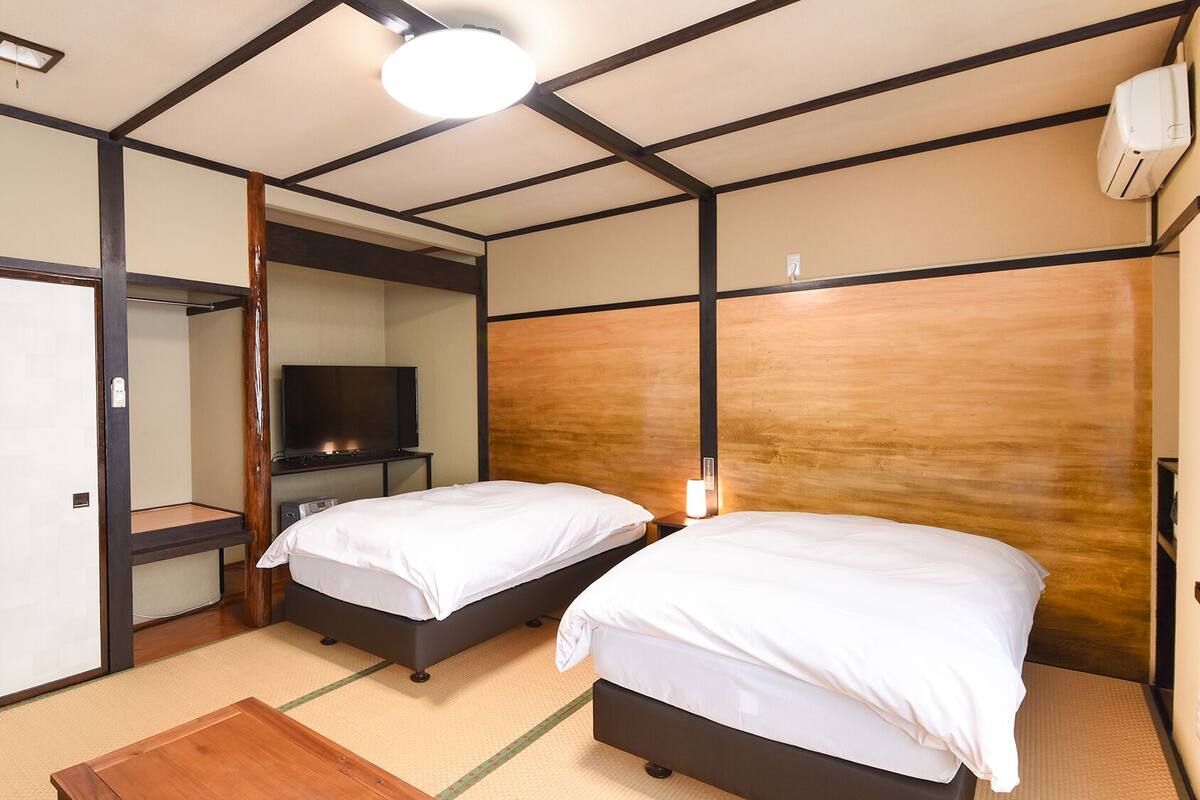 Una habitación de hotel con dos camas, televisión, armario y una lámpara en el techo.