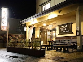 Un edificio con entrada cubierta, mesas al aire libre y un letrero con texto en japonés.