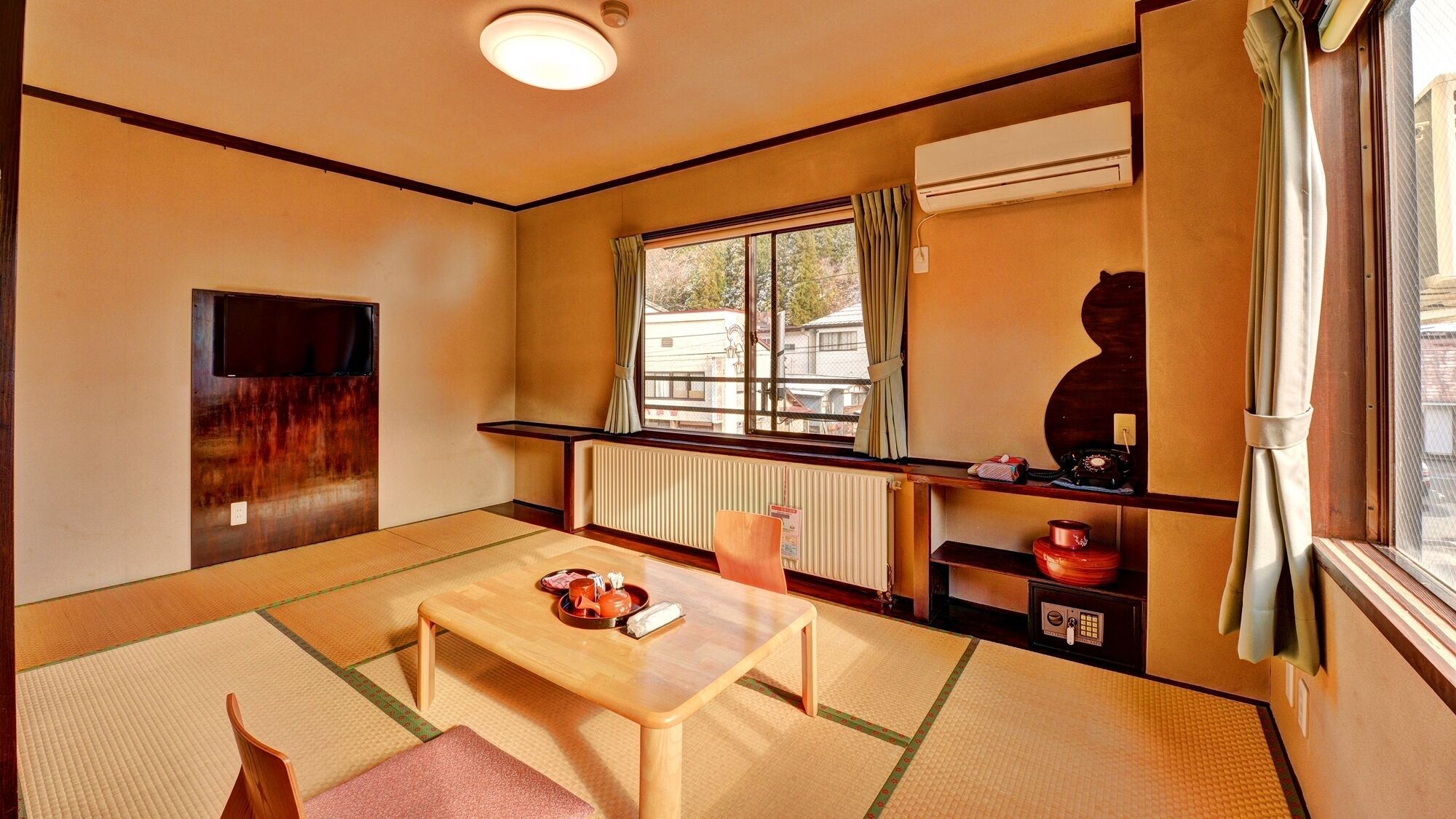 Una habitación tradicional japonesa con suelo de tatami, una mesa de madera baja, un televisor y una ventana con cortinas.