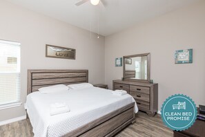 Une chambre à coucher propre et moderne, avec un lit en bois, une table de chevet, une commode et un ventilateur de plafond.