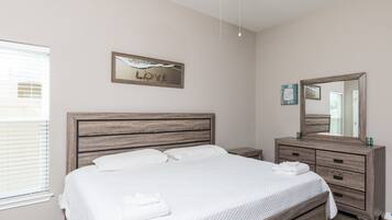 A clean, modern bedroom with a wooden bed, a nightstand, a dresser, and a ceiling fan.