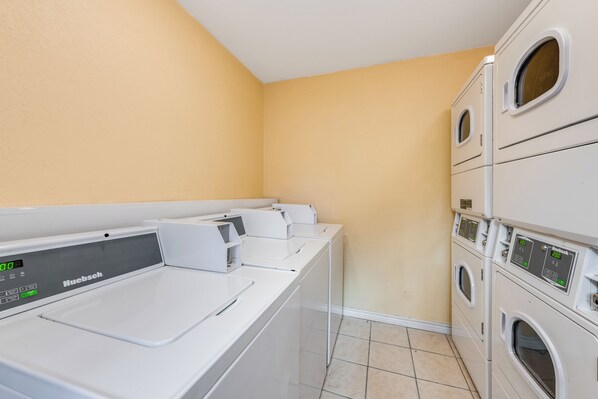 A laundry room with a white Huebsch washing machine and dryer, beige walls, and tiled flooring.