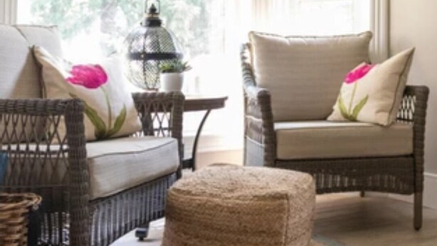 Una habitación acogedora con muebles de mimbre, un banco acolchado y una alfombra estampada.