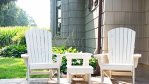 Dos sillas Adirondack blancas y una pequeña mesa en un patio de ladrillo.