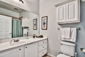 Ein Badezimmer mit einem weißen Waschbecken, einem Spiegel und einer Toilette. An der Wand hängen zwei Bilder und ein Handtuchhalter mit Handtüchern.