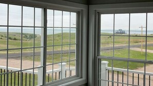 Een kamer met twee grote ramen met uitzicht op een landelijk landschap met velden en een weg.
