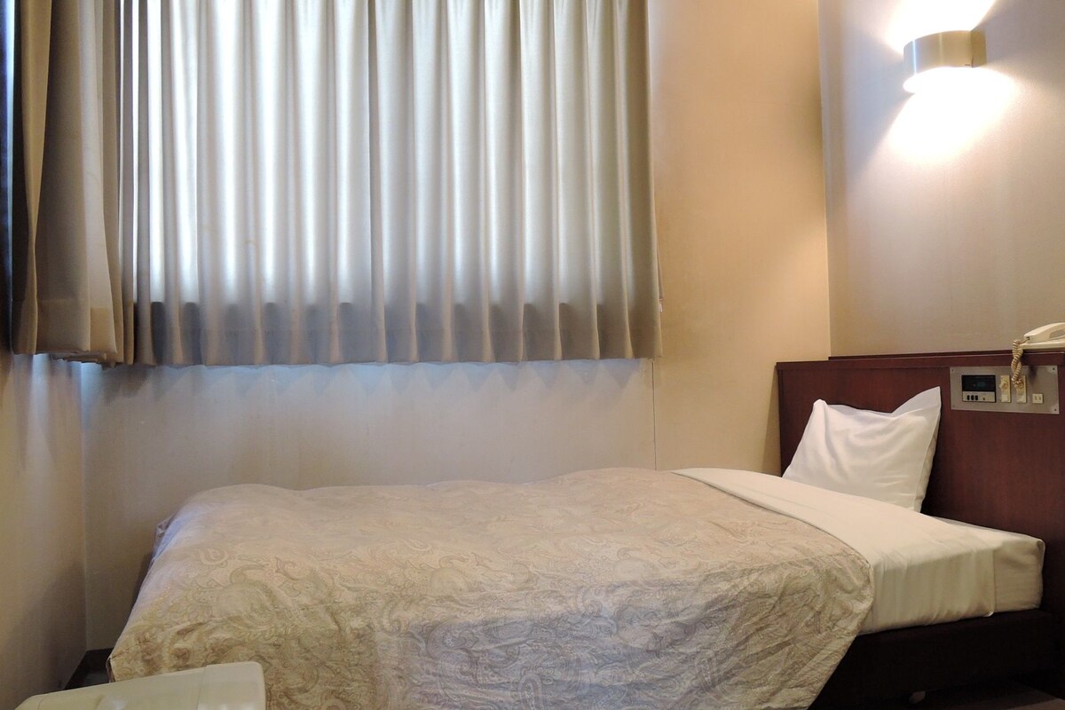 A hotel room with a bed, a bedside telephone, and a wall-mounted light fixture.