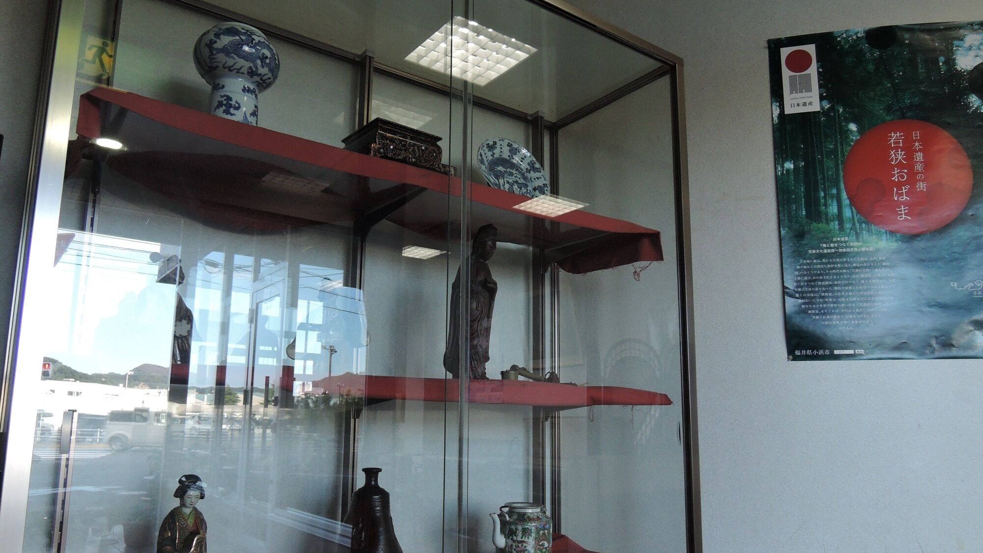 A glass display case with traditional Japanese artifacts, including a vase, a statue, and a teapot.