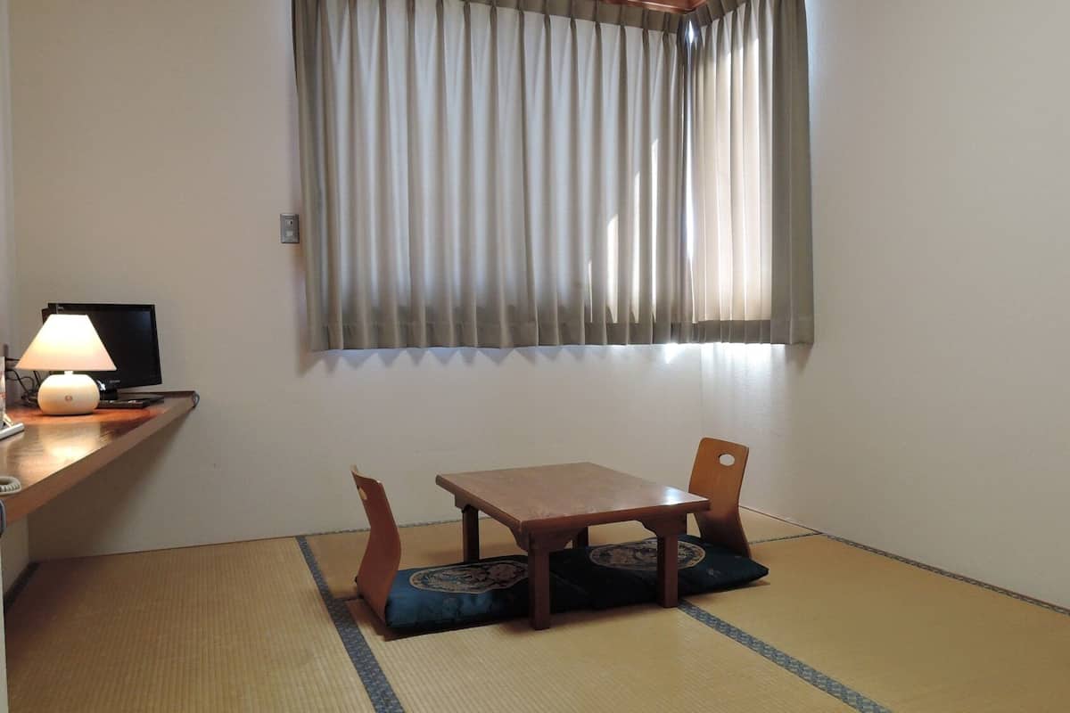 A small room with a wooden table and chairs, a lamp, and a window with curtains.