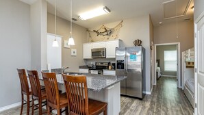 A modern kitchen with granite countertops, stainless steel appliances, and wooden chairs. - Family Beach Townhome | 2 Pools & Walk to Beach (Corp Christi)