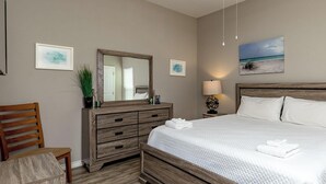 A clean, well-lit bedroom with a large bed, wooden headboard, a dresser, a chair, and a nightstand with a lamp. - Family Beach Townhome | 2 Pools & Walk to Beach (Corp Christi)