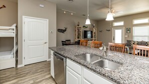 A kitchen with granite countertops, a dishwasher, and a dining area with wooden chairs and a table. - Family Beach Townhome | 2 Pools & Walk to Beach (Corp Christi)