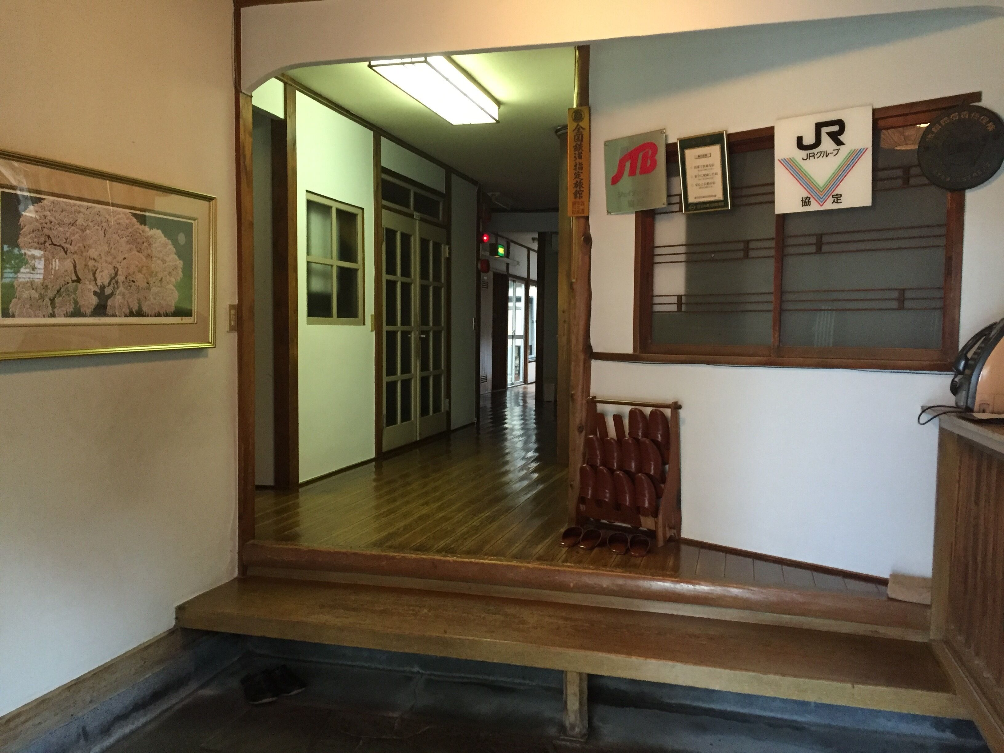 A hallway with wooden flooring, a framed picture on the left, a shoe rack, and various signs on the wall.