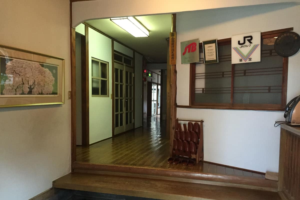 A hallway with wooden flooring, a framed picture on the left, a shoe rack, and various signs on the wall.