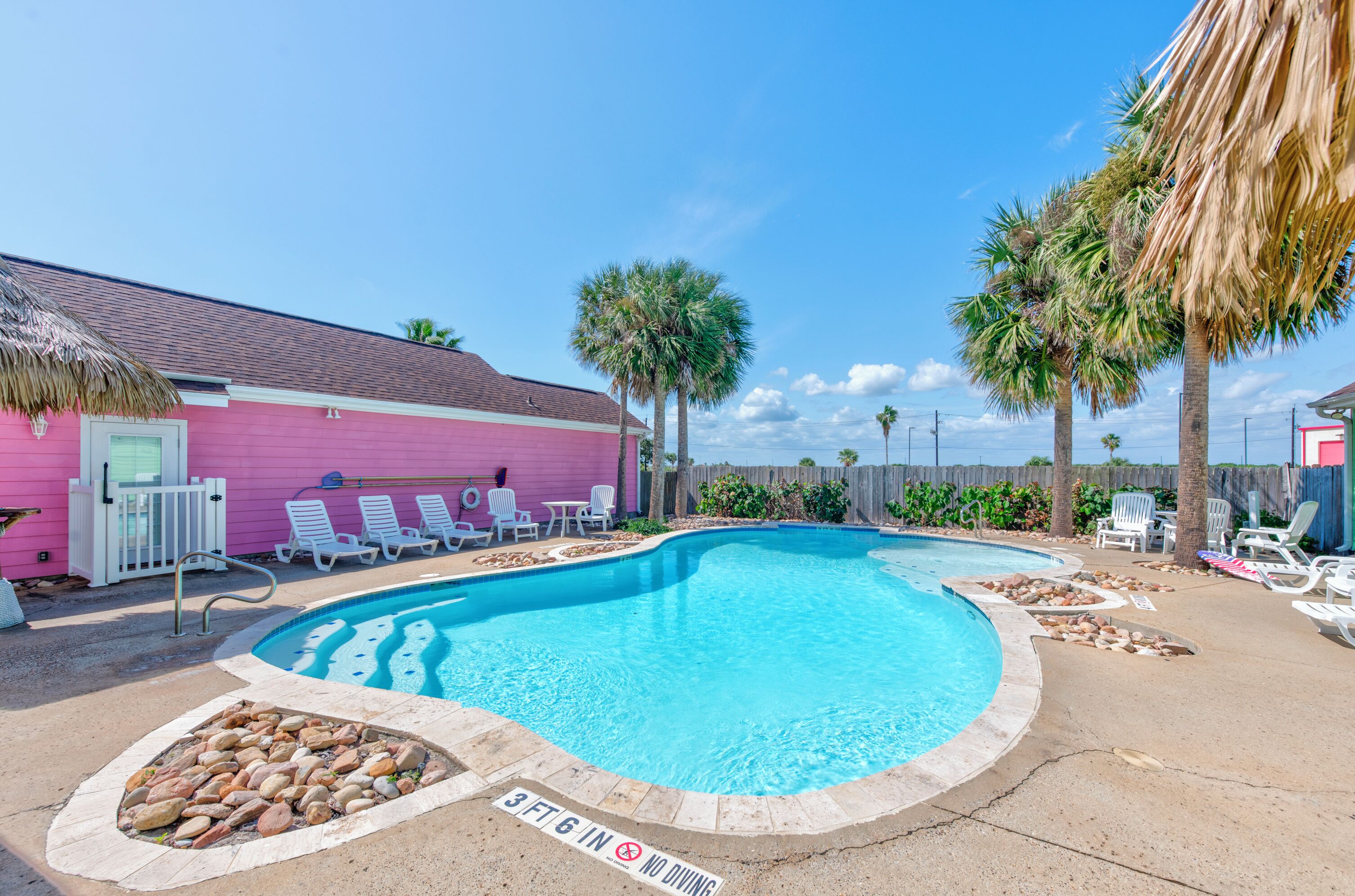 A swimming pool with lounge chairs and a pink building in the background.
