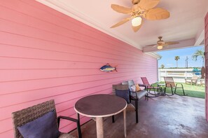 A covered patio with pink siding, a round table, wicker chairs, and ceiling fans. - Dog-Friendly Cottage | Sparkling Pool, Patio & Turf Grass (Corpus Christi)