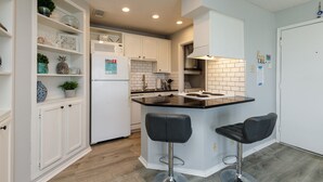 A modern kitchen with white cabinetry, a black countertop island, and two bar stools. - Relaxing Gulf Coast Condo with Pool, Hot Tub & Balcony (Corpus Christi)