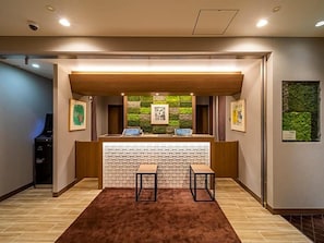 Un área de recepción con mostrador de madera, dos sillas, un papel tapiz decorativo y un elemento decorativo en la pared verde.