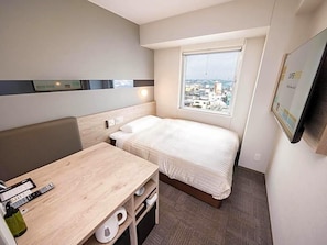 A hotel room with a bed, a desk, a chair, a window with a city view, and a mounted television. - Super Hotel Marugame Station Front (Marugame)
